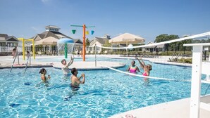 Ett poolområde med en vattenlekplats, solstolar och en avskärmad sittplats.