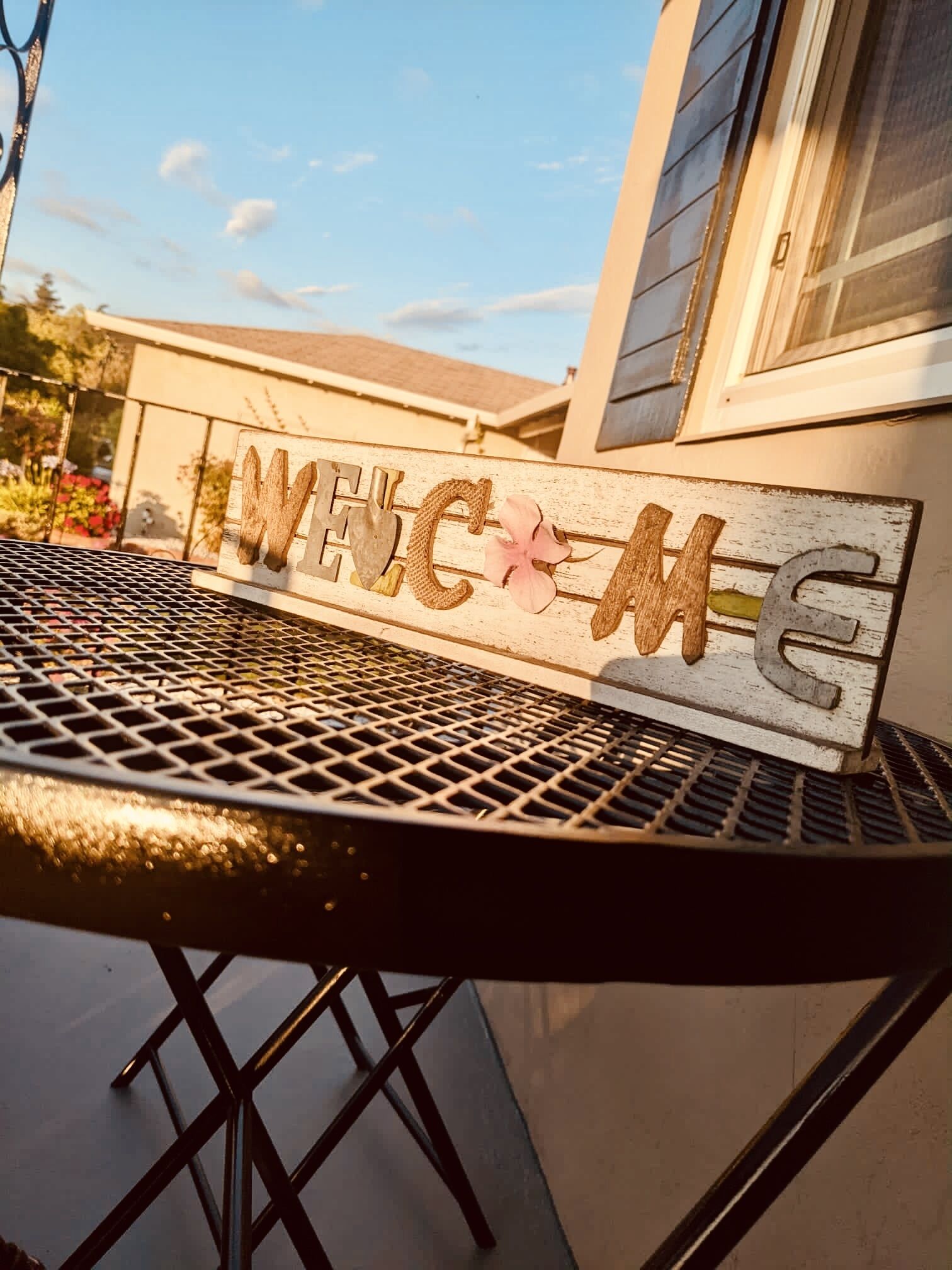 Une table en métal sur laquelle est posée une pancarte indiquant « BIENVENUE », avec des lettres et une fleur.