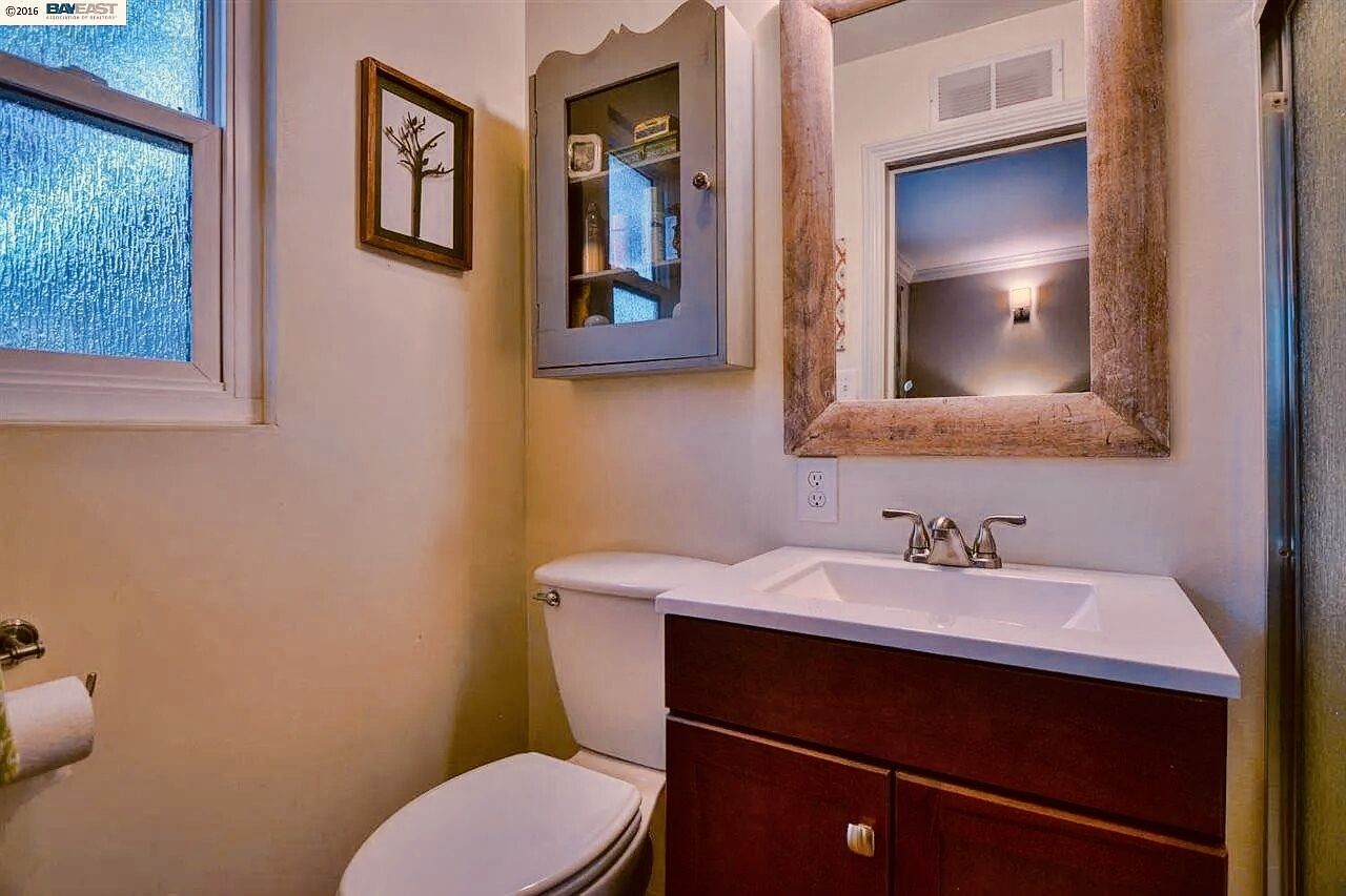 A bathroom with a toilet, sink, vanity, and a mirror.