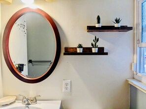 Un baño con un espejo redondo, un lavamanos y dos estantes con plantas en macetas.