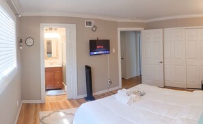 Habitación de hotel con cama, televisor montado en la pared, puerta y ventana con persianas.