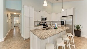 Una cocina moderna con armarios blancos, encimera de granito, electrodomésticos de acero inoxidable y una isla central con taburetes de bar.