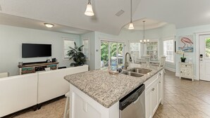 Una cocina amplia con encimera de granito, armarios blancos, lavavajillas integrado y una isla grande con fregadero.