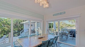 A dining area with a wooden table and chairs, large windows, and a view of the outdoors. - Mermaid's Crossing managed by Beach Retreats (Holmes Beach)