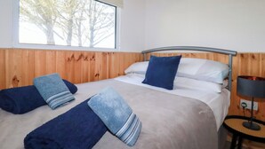 Una habitación con cama, ventana que da a árboles y lámpara sobre una mesita.