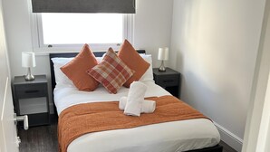 Una camera da letto ordinata con un letto, due comodini, una finestra con persiana e un pavimento in legno.