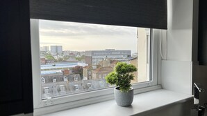 Un bagno con una finestra che si affaccia su una vista urbana, una pianta in vaso sul davanzale e un rubinetto moderno.