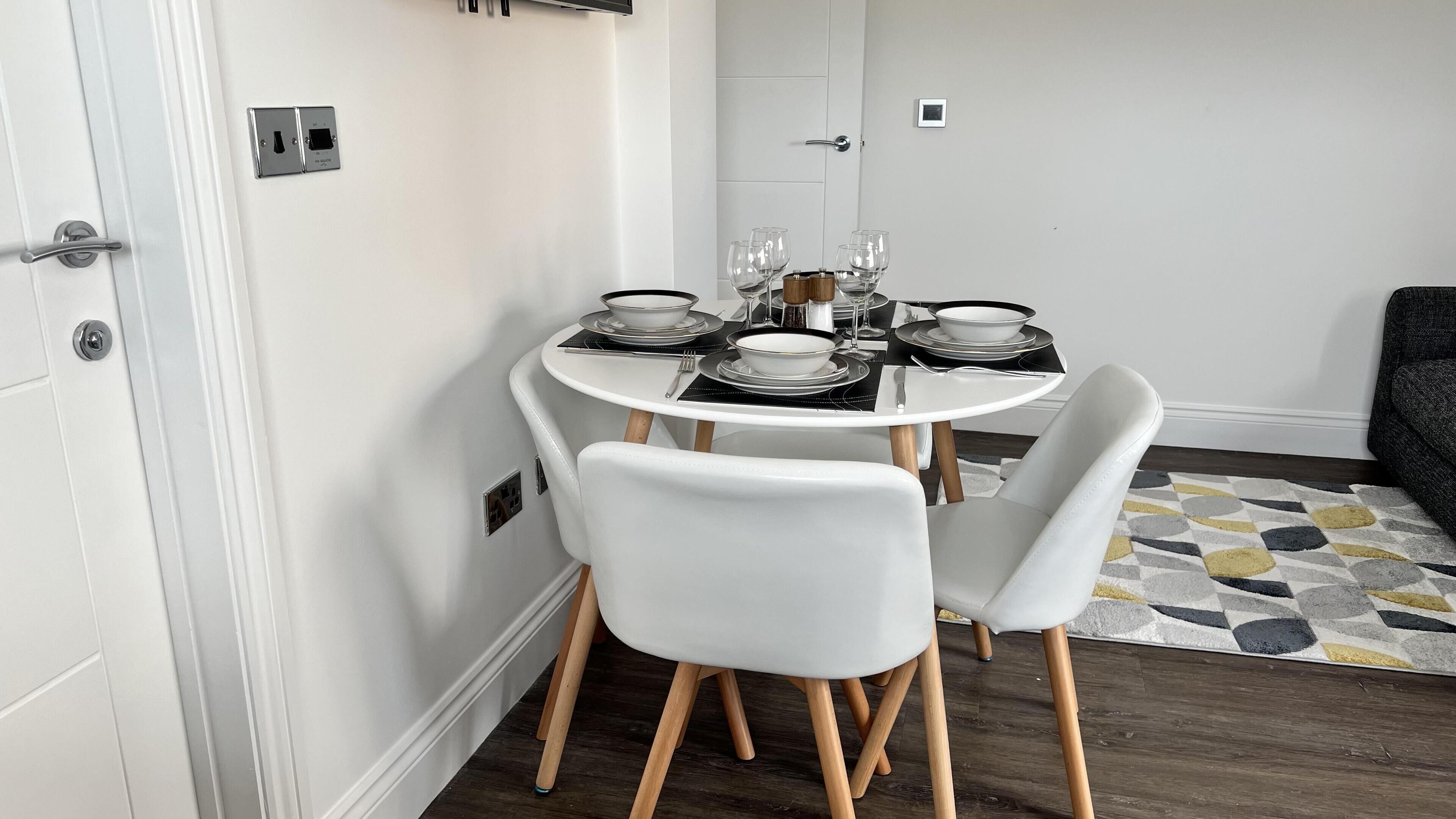 Un comedor con una mesa redonda dispuesta para cuatro personas, sillas blancas y un tapete estampado.