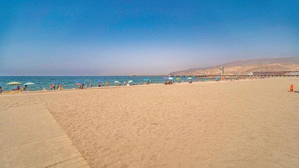 Une vaste plage de sable, parsemée de parasols et fréquentée par de nombreuses personnes.