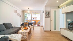 Un salon moderne comprenant un canapé, une table à manger et des chaises. On y trouve également un coin cuisine avec des placards et un téléviseur.