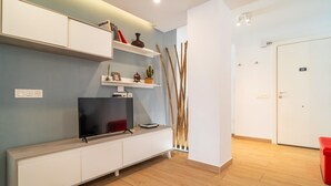 Un salon moderne avec un téléviseur à écran plat posé sur une console blanche, des étagères ornées d’objets décoratifs et un plancher en bois.