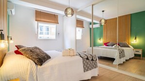Une chambre avec un grand miroir, deux lits, une fenêtre avec des stores et un plancher en bois.