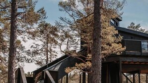 A wooden staircase leading to a covered outdoor area with a modern building in the background. - Luxurious Tree Top Cabin by the Lake (Iveland)