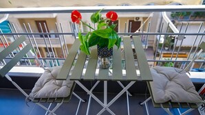 Un balcon avec une balustrade en métal, une petite table sur laquelle est posé un vase de fleurs et deux coussins.