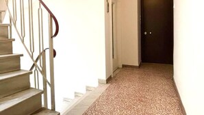 Un escalier avec des rampes en métal mène à une porte sombre au bout d’un couloir dont le sol est recouvert d’un motif à points.