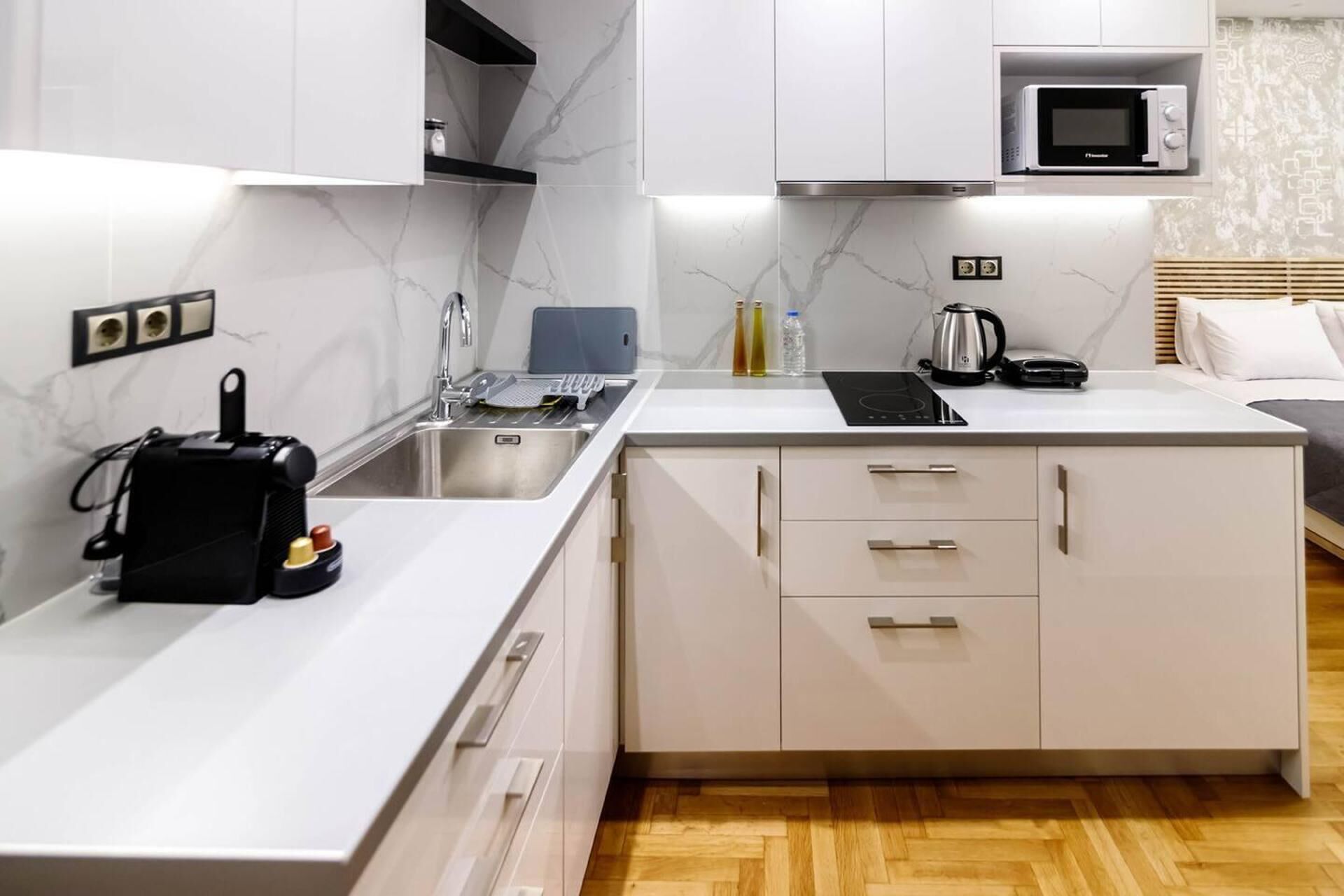 Une cuisine moderne avec des meubles blancs, un four à micro-ondes encastré, une bouilloire et un grille-pain.