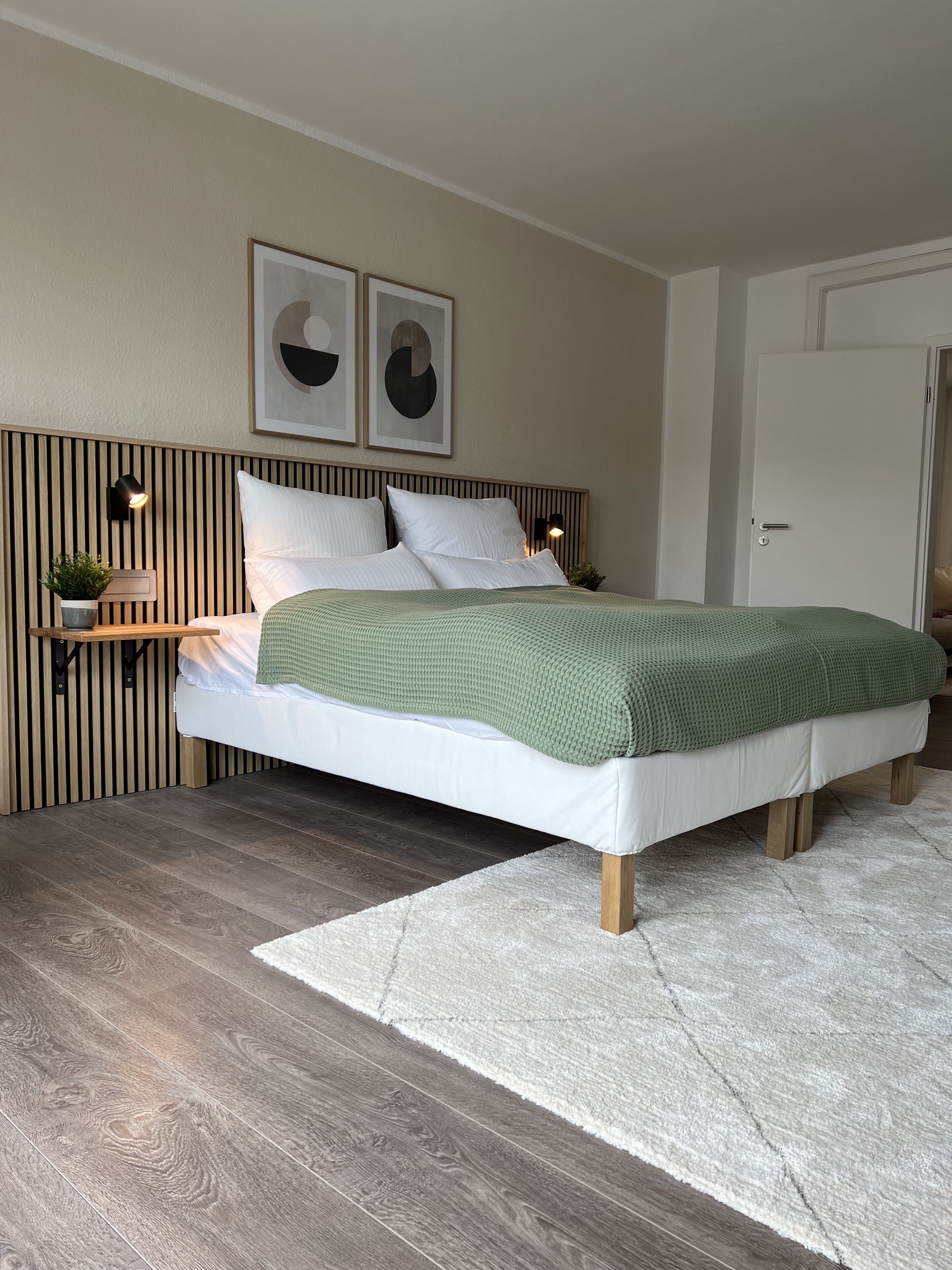 A modern bedroom with a wooden headboard, a green blanket, and a white rug.