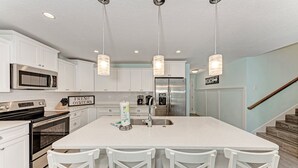 A modern kitchen with white cabinetry, stainless steel appliances, and a central island with bar stools. - Turtle's Bay managed by Beach Retreats (Holmes Beach)