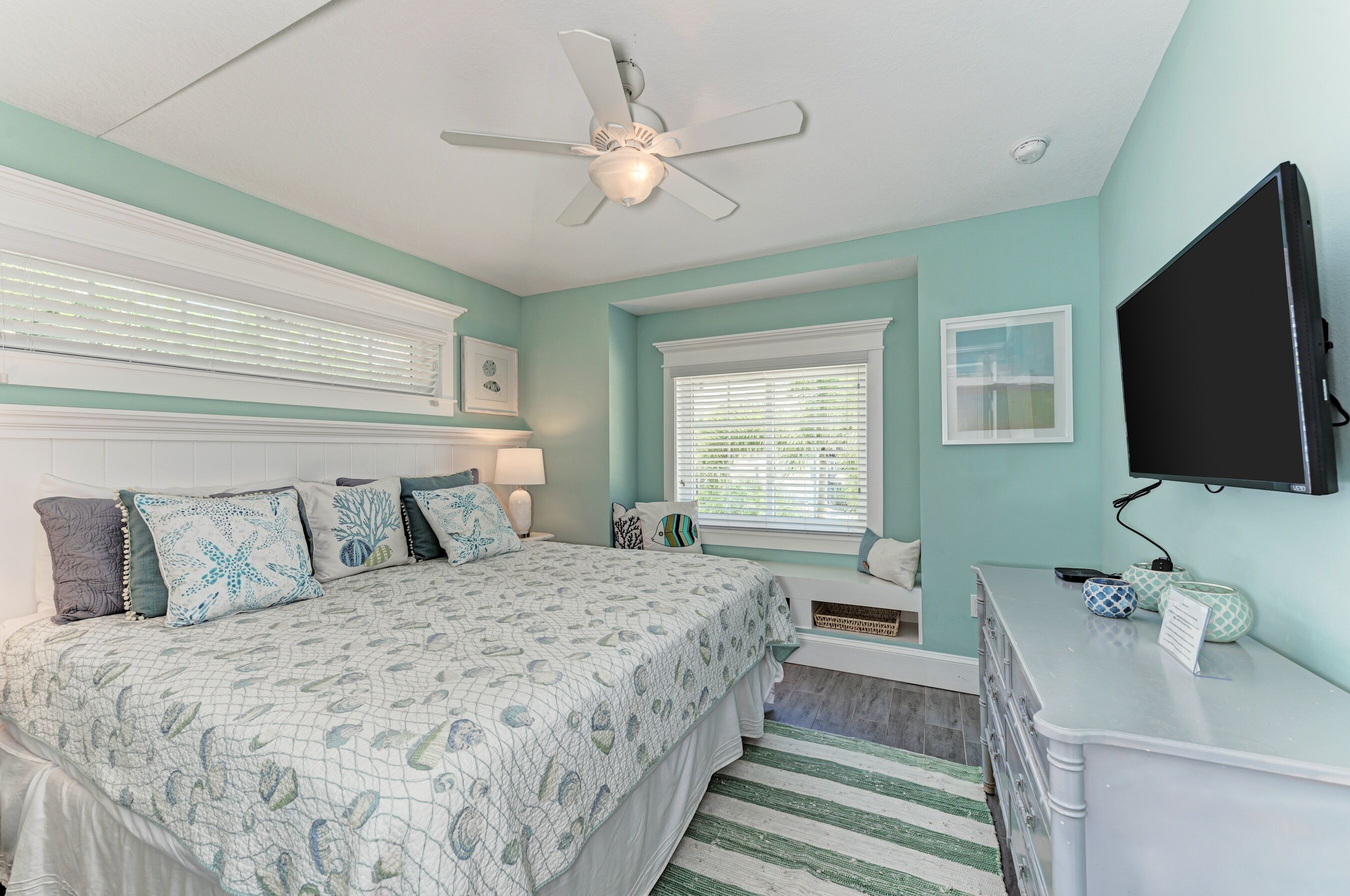 A bedroom with a bed, a ceiling fan, a TV, and a window with blinds.