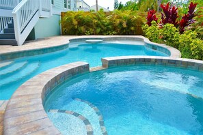 Ein Pool mit geschwungener Form, umgeben von einer Steindeck und üppiger Vegetation.