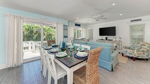 A dining area with a table set for four, a blue sofa, and a television in the background. - Turtle's Bay managed by Beach Retreats (Holmes Beach)