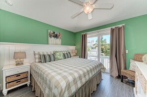 A bedroom with a bed, nightstands, a ceiling fan, and a view of the outdoors. - Turtle's Bay managed by Beach Retreats (Holmes Beach)