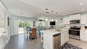 A spacious kitchen with white cabinetry, a large island, stainless steel appliances, and a dining area with a view to the outdoors. - Turtle's Bay managed by Beach Retreats (Holmes Beach)