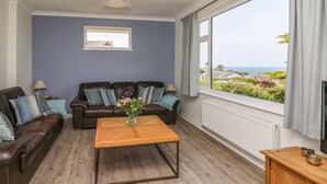 Un salon avec un canapé en cuir marron, une table basse en bois et une vue sur la mer, visible à travers une grande fenêtre.