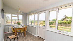 Un coin repas avec une table dressée pour quatre personnes, de grandes fenêtres donnant sur la campagne et un plancher en bois.