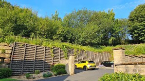 Ein gelber SUV vor einem Eingangstor mit Steinmauer und Grünpflanzen.