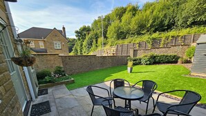 Eine Terrasse mit Tisch und Stühlen, eine kleine Rasenfläche und eine Mauer aus Stein.