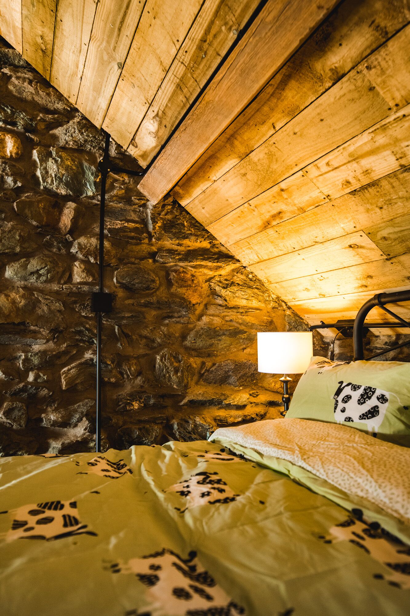 A cozy room with a stone wall, wooden ceiling, and a bed with patterned bedding.