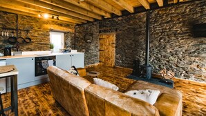 Ein rustikales Interieur mit freiliegenden Holzbalken, einer Steinwand, einer Küchenzeile und einer Sitzecke mit Kamin.