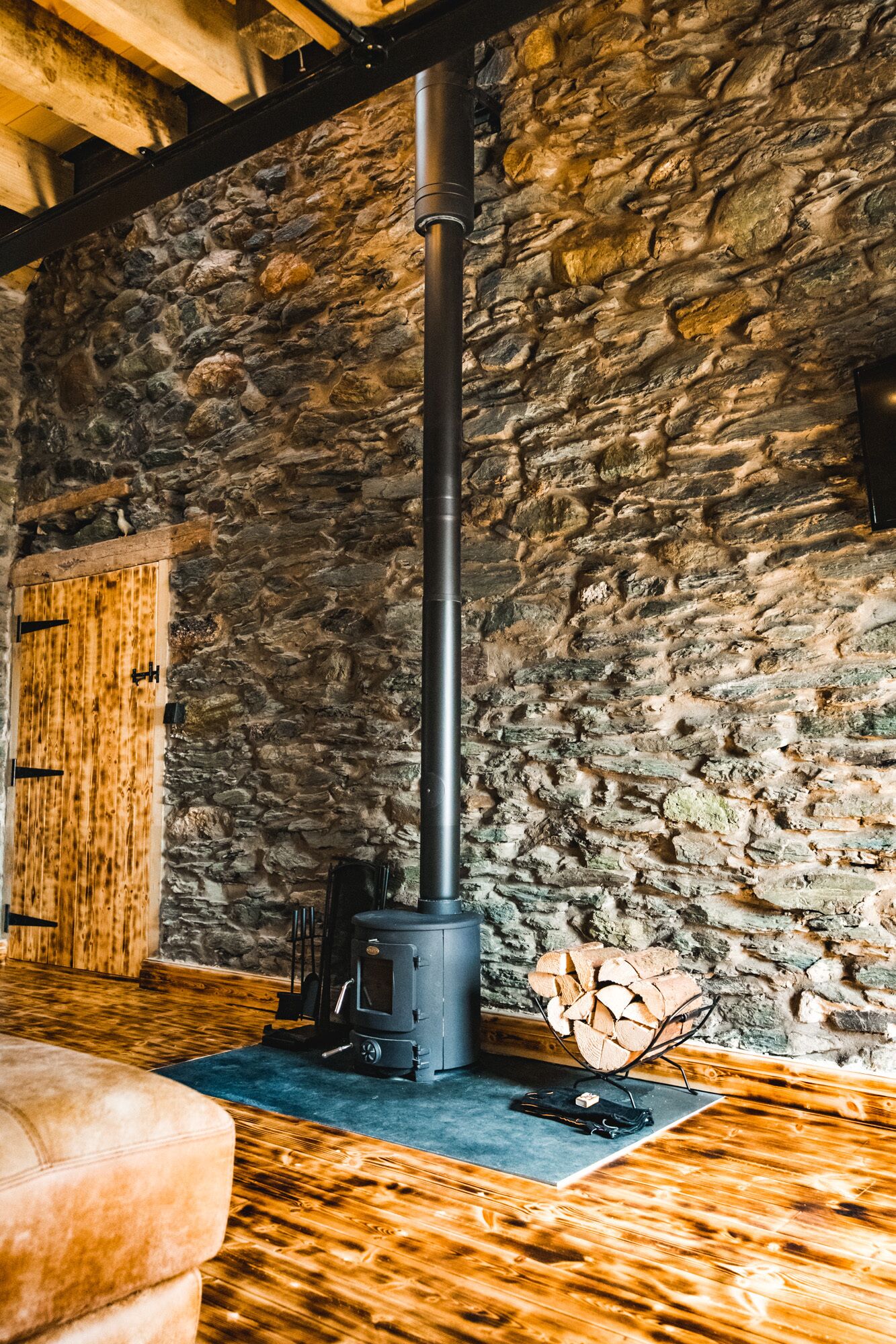 A rustic interior with a stone wall, a wooden bench, and a black wood stove.