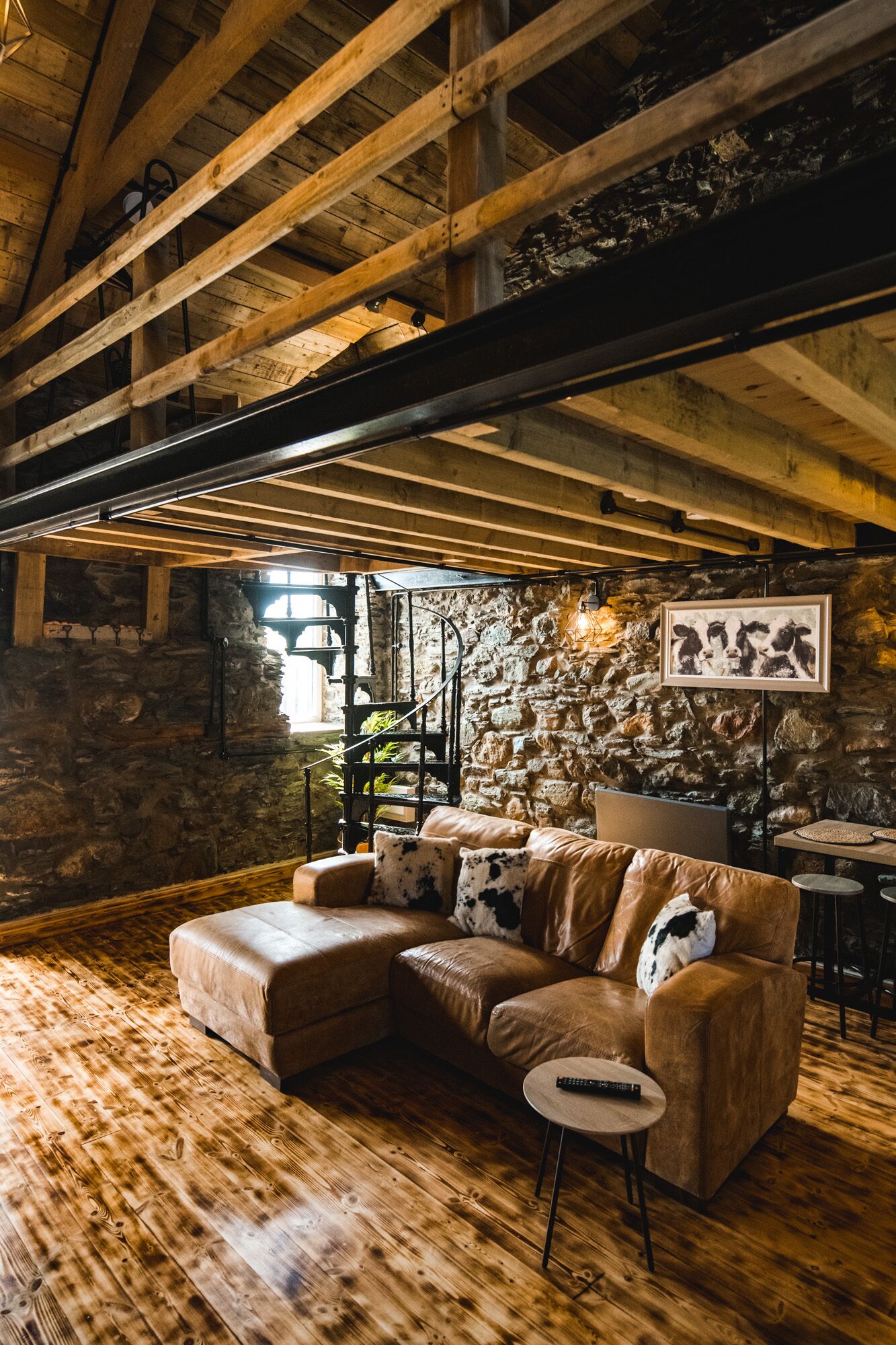 A rustic interior with exposed wooden beams, a stone wall, and a leather sofa with cowhide pillows.
