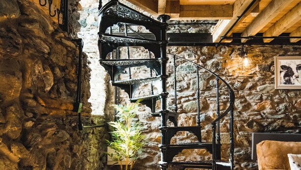 Eine Wendeltreppe in einem rustikalen Raum mit Steinwänden und Holzdielen.