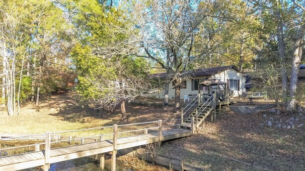A cabin with a wooden deck and a small bridge over a pond, surrounded by trees. - Lake Wateree cottage (Ridgeway)