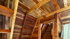 Een kleine, houten kamer onder een schuin dak, met een wit toilet, een kleine, witte koelkast en een houten stoel.