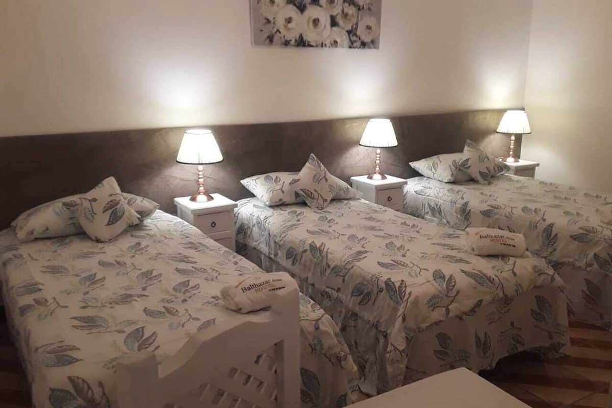 A hotel room with two single beds, each with a floral bedspread and matching pillows. There are bedside tables with lamps and a small table in the center.