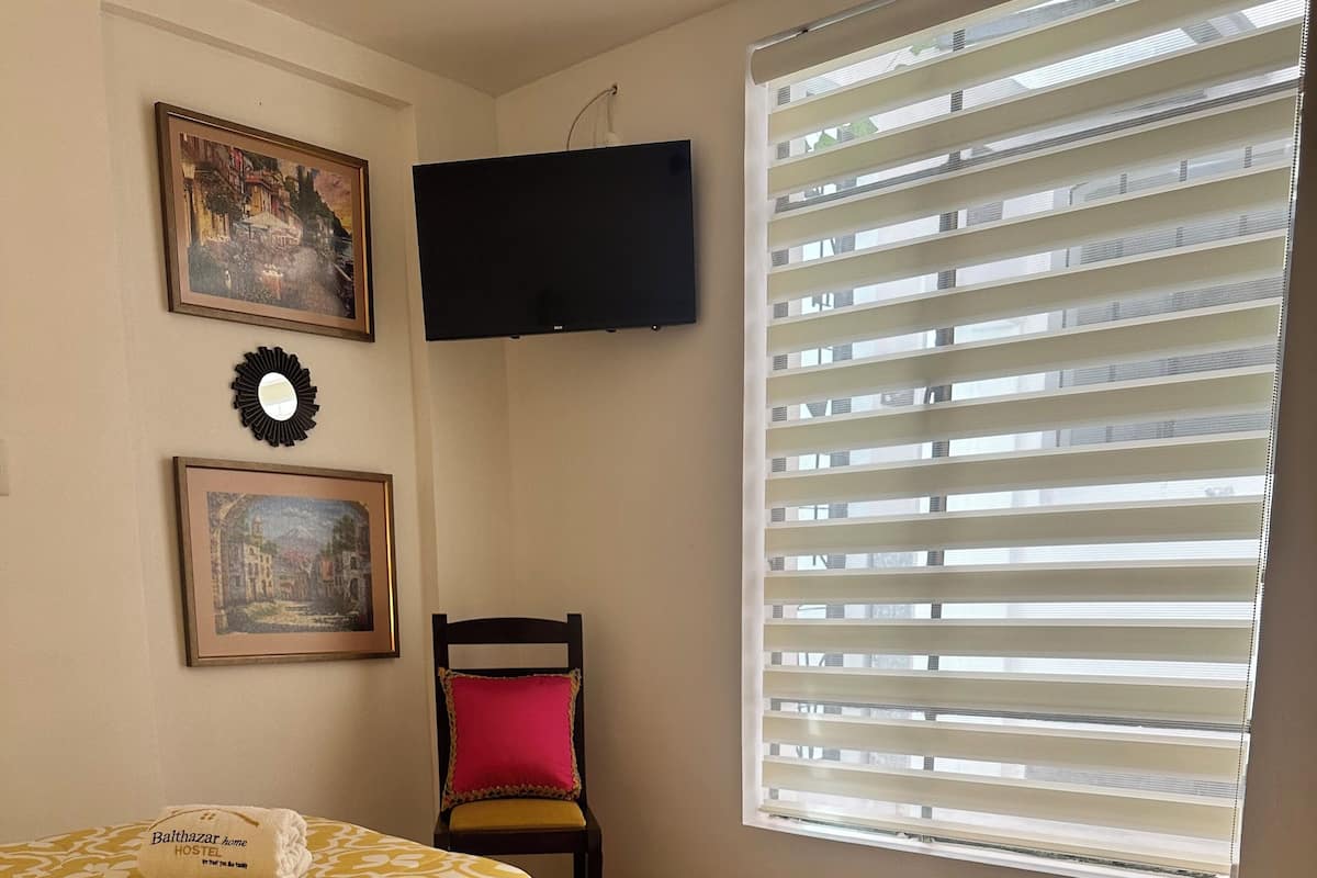 A hotel room with two beds, a TV mounted on the wall, and a window with blinds.