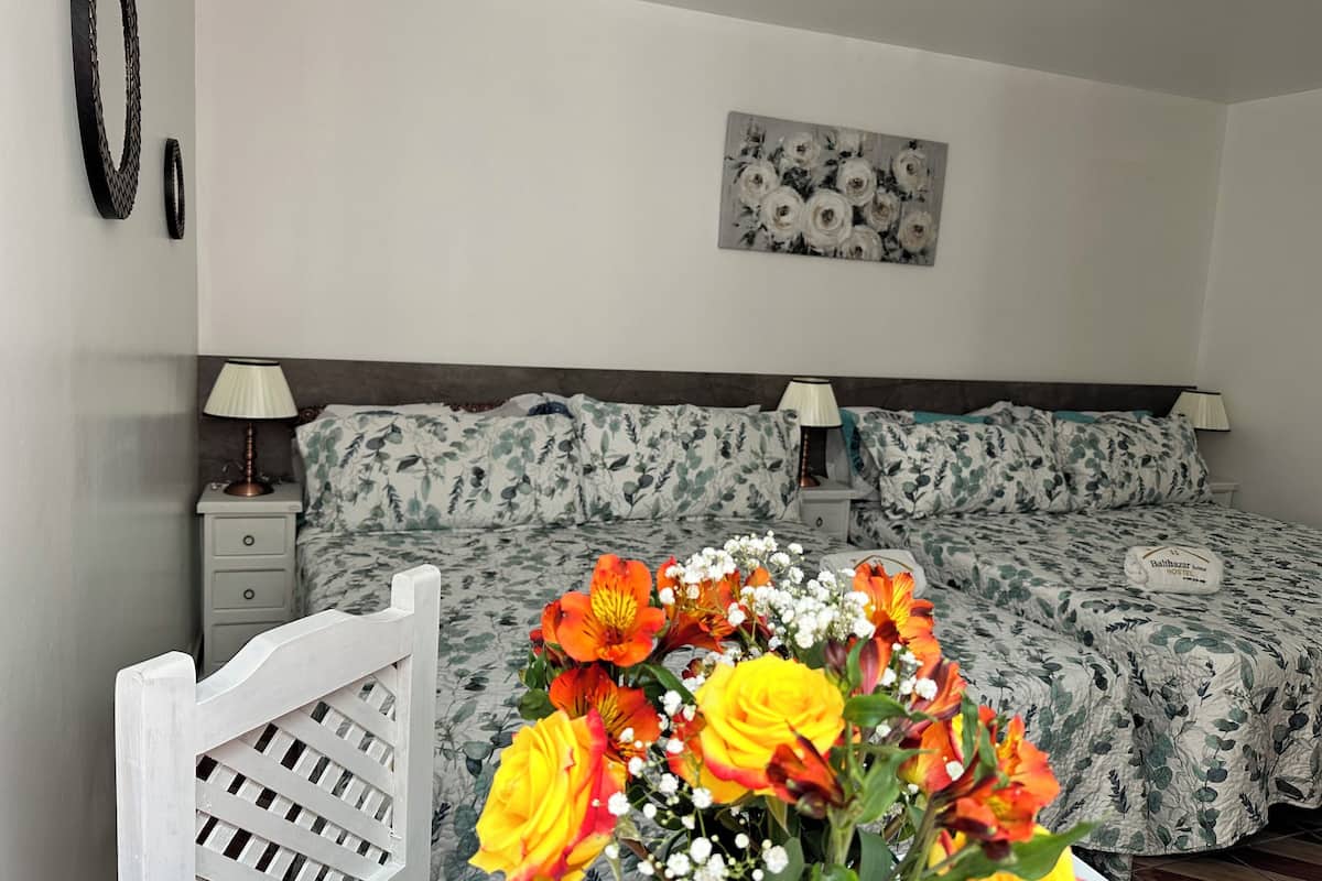A bedroom with a bed, two bedside tables, a nightstand, a white chair, and a floral wall decoration.