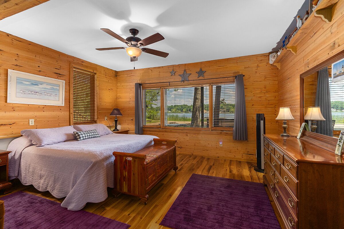 A wooden cabin bedroom with a bed, dresser, and ceiling fan.
