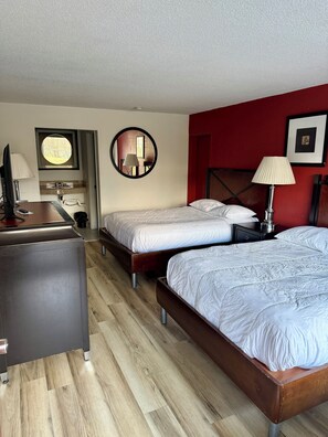 A hotel room with two beds, a desk, a mirror, and a red accent wall. - Virginian Motel (Stuart)