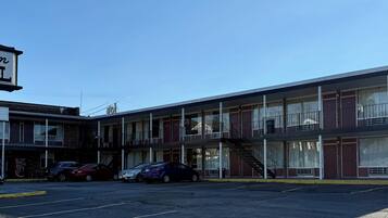 Un motel con un letrero que dice 'Virginian MOTEL' y un letrero de 'VACANCY'. Hay coches estacionados al frente, y el edificio tiene varios pisos con ventanas y balcones.