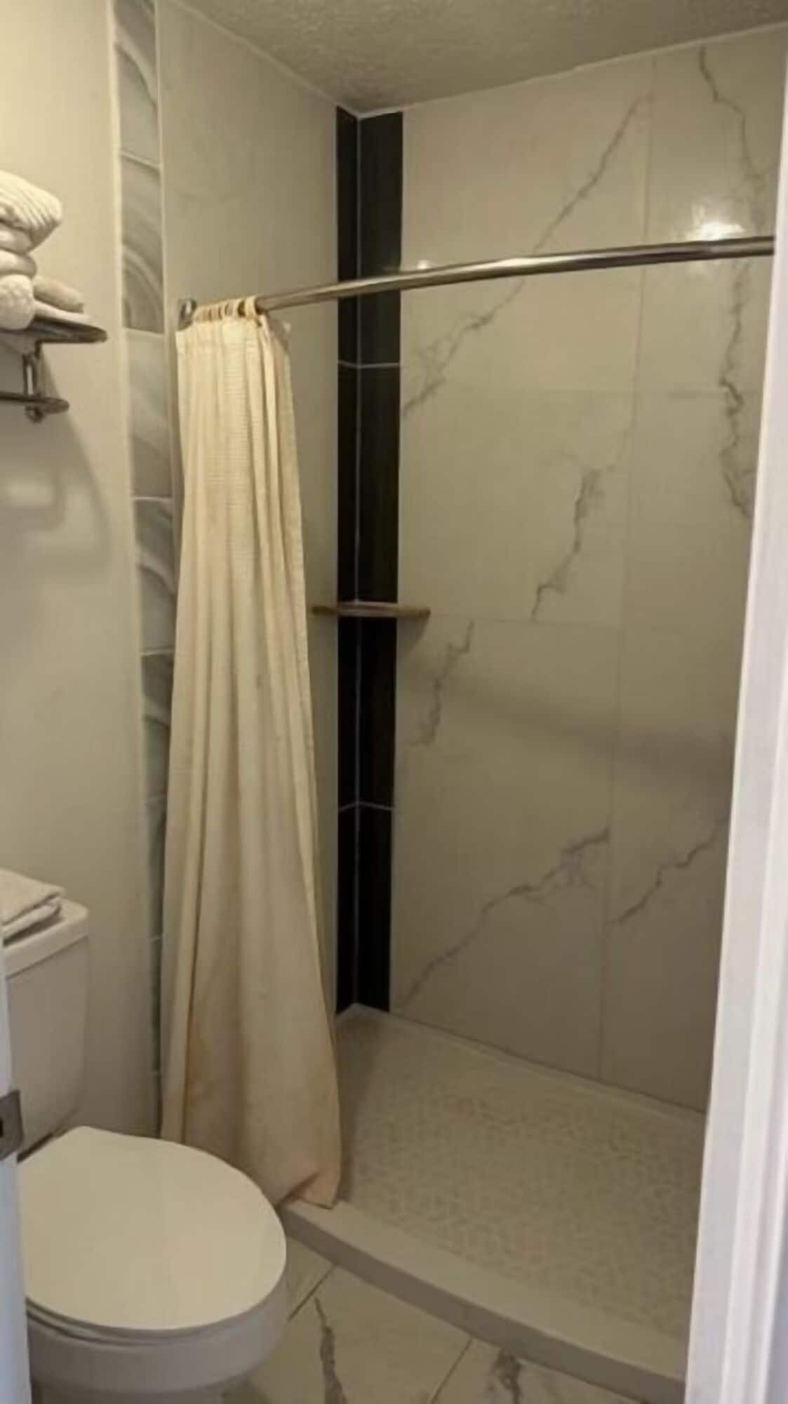 Een badkamer met een douche, toilet en handdoekrek.