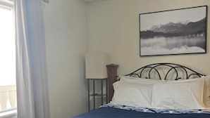 Un lit avec une couvre-lit bleue, une tête de lit en bois, une table de chevet avec une lampe et un tableau encadré au mur.