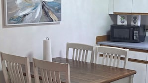Une table à manger avec quatre chaises, un four à micro-ondes et un tableau accroché au mur.