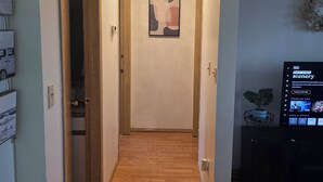 Un couloir doté d’un plancher en bois, d’un luminaire au plafond, d’un tableau abstrait encadré et d’un téléviseur affichant l’interface d’un service de diffusion en continu.