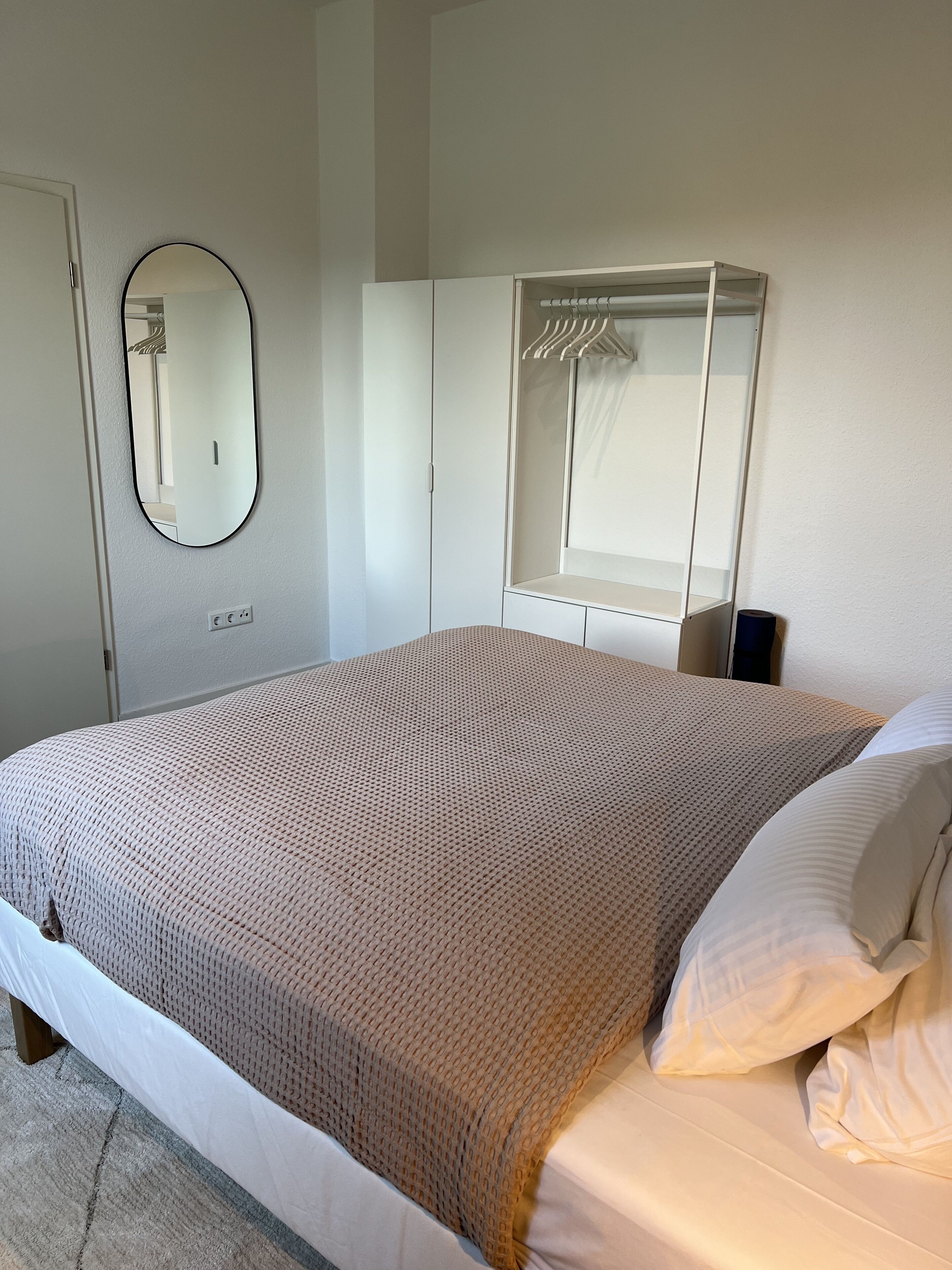Ein Schlafzimmer mit einem Bett, einem Kleiderschrank, einem Spiegel und einer Garderobe.