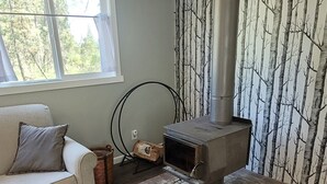 A cozy living room with a wood-burning stove, a sofa, a patterned rug, and a window with a view of trees. - Spokane Chalet WIFI included (Spokane)